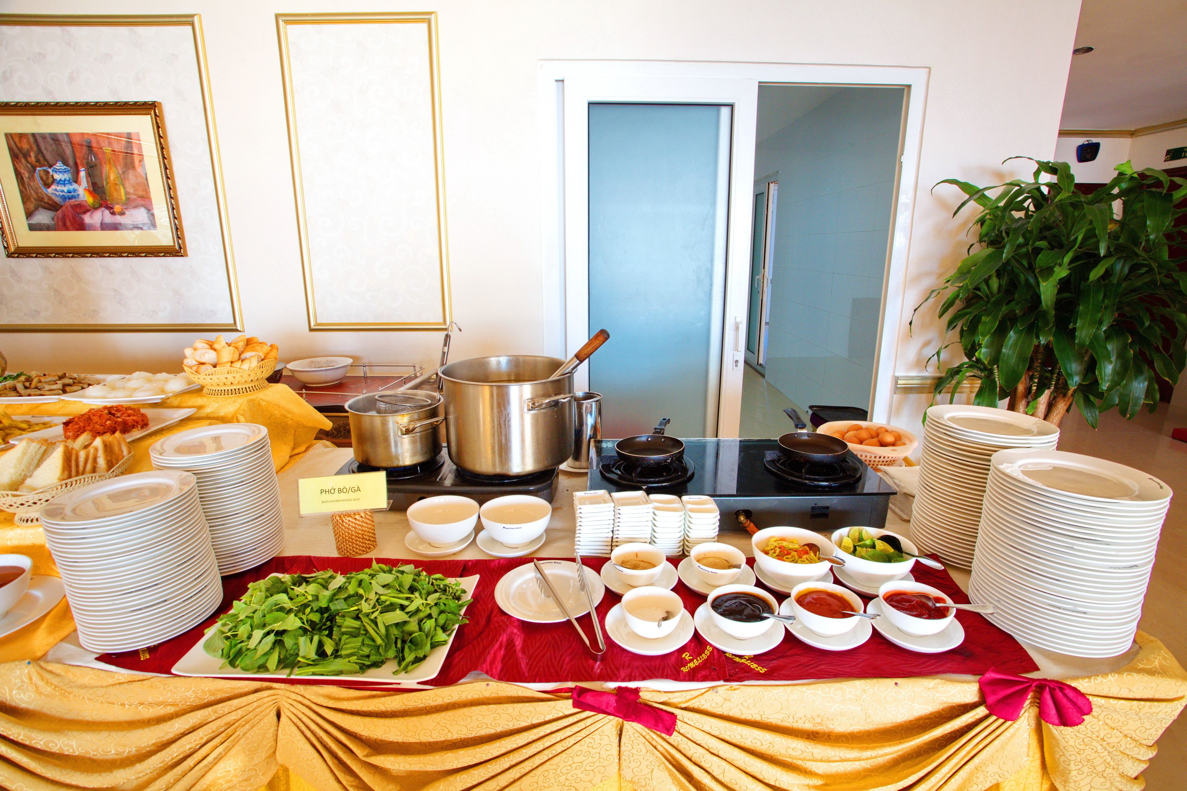 A buffet setup with various dishes, bowls, and plates arranged on a table with a red cloth.