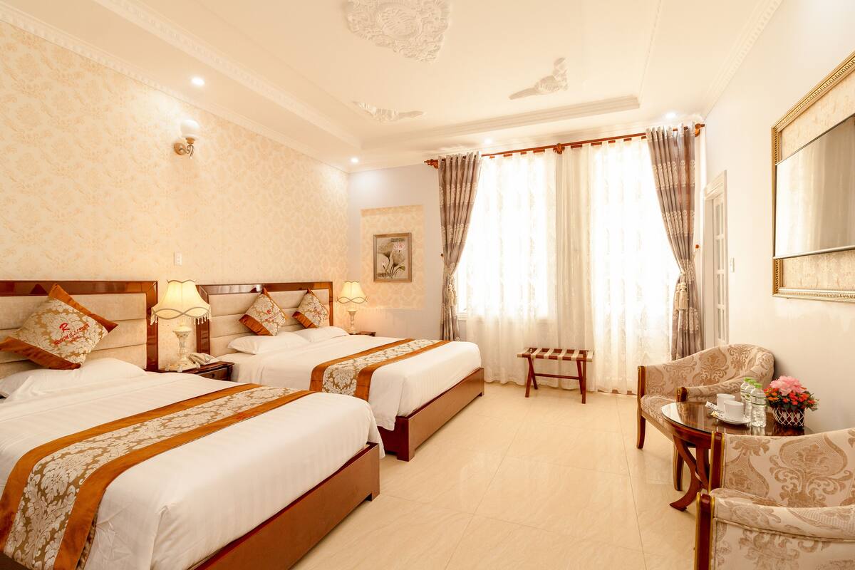 A hotel room with two beds, a sitting area with a table and chairs, and a large window with curtains.