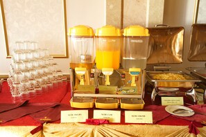 Dispensadores de bebidas identificados para chá verde, sumo de laranja e sumo de limão, dispostos num buffet.