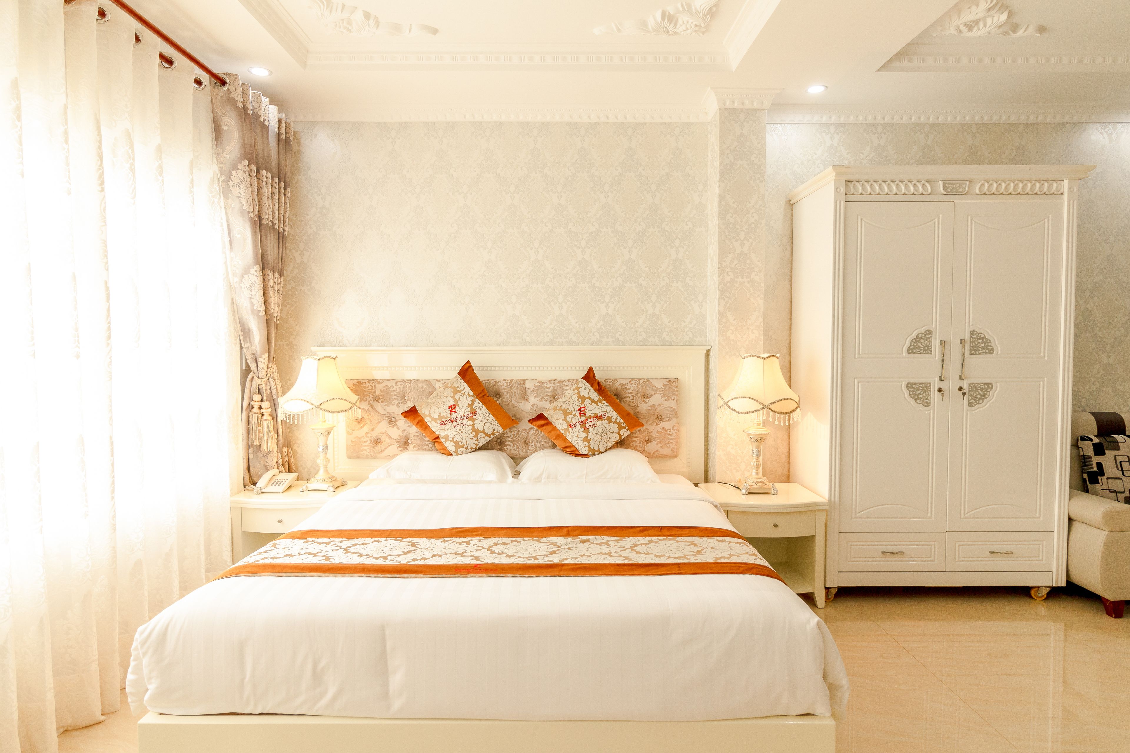 Un dormitorio bien iluminado con una cama grande, dos mesitas de noche, un armario y un cabecero decorativo.