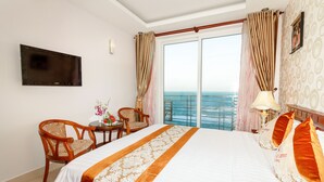 A hotel room with a bed, a TV, a table with chairs, and a view of the sea. - Romeliess Hotel (Ho Chi Minh City)