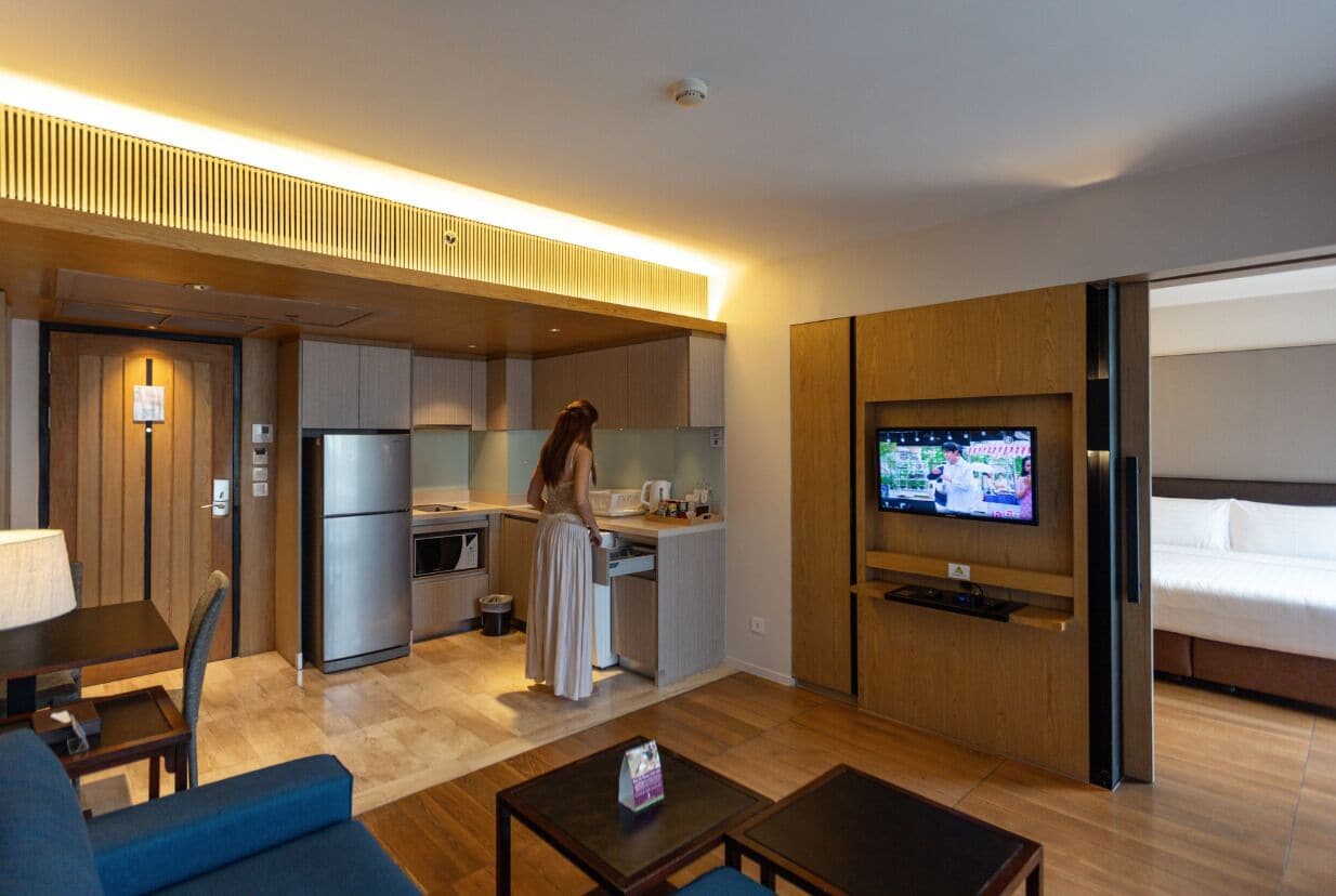 A compact hotel room with a kitchenette, a TV, a sofa, and a bed.