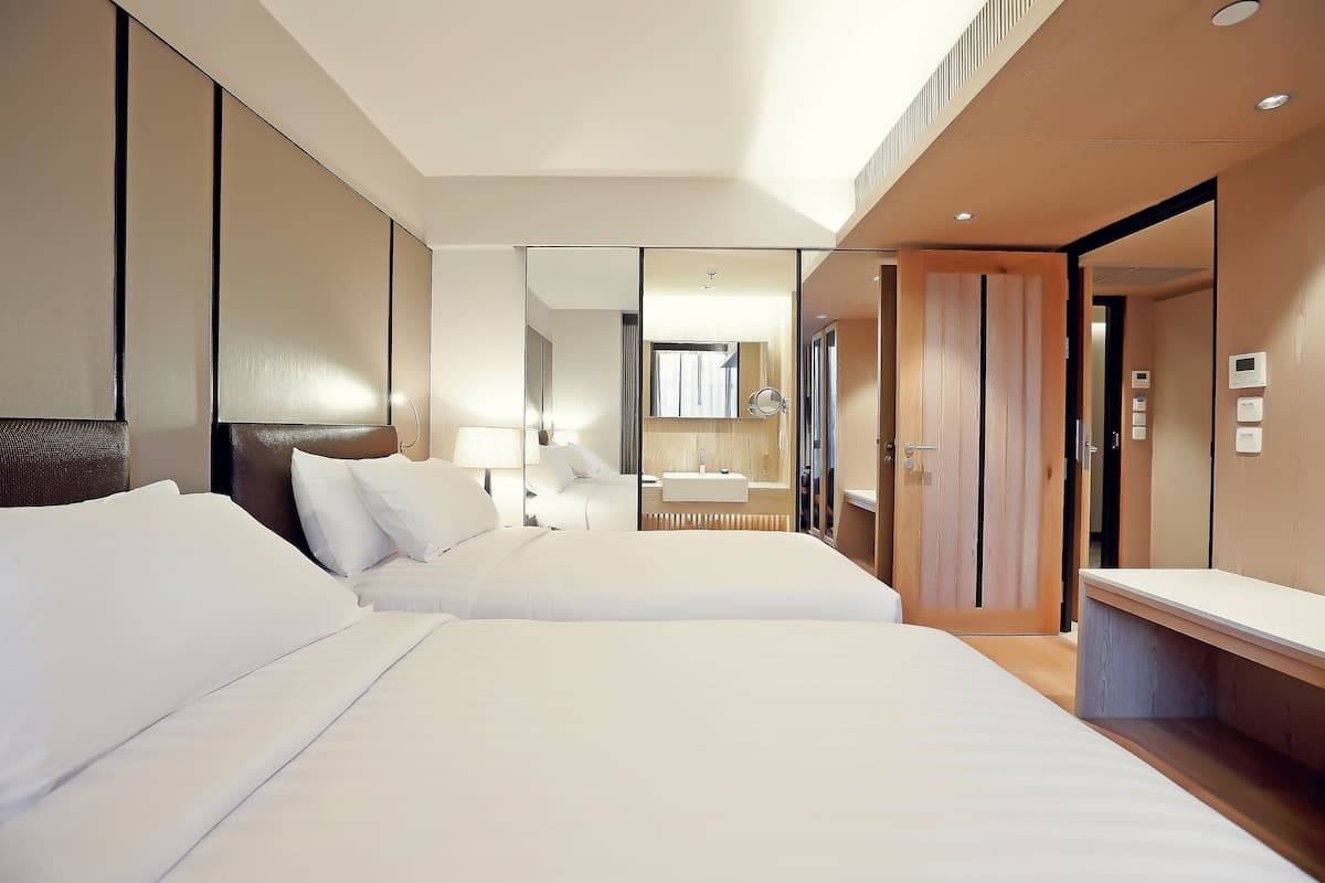 Habitación de hotel moderna con dos camas, un espejo grande, una mesita de noche y un armario de madera.