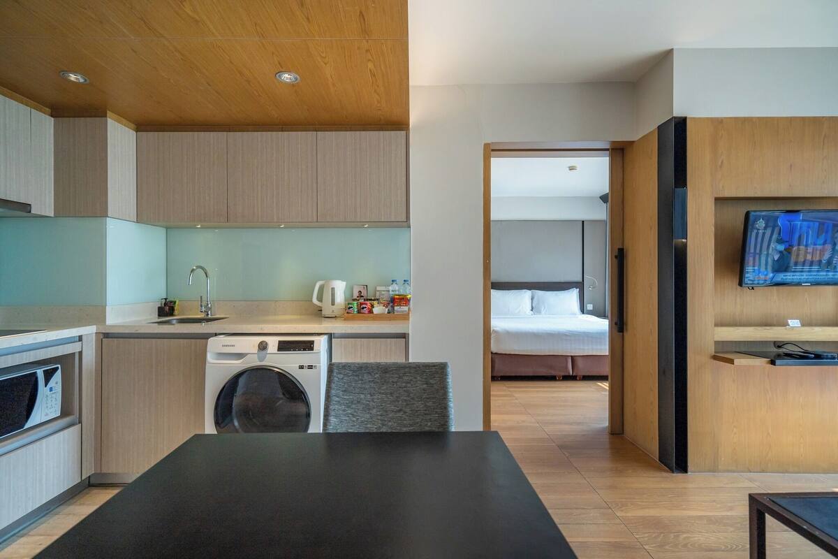 Una habitación de hotel moderna con kitchenette, lavadora, comedor y cama.