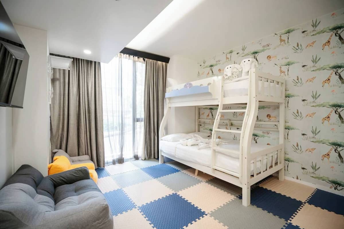 Una habitación con literas, un sofá y un ventanal con cortinas.