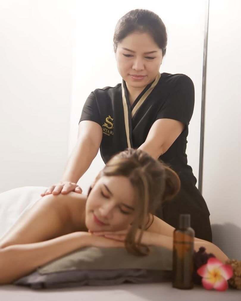 Eine Massageanwendung in einem Raum mit Massageliege, einer Flasche und einer Blume.