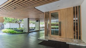 A modern building with a wooden slatted ceiling, a glass door entrance, and a courtyard with plants and seating.