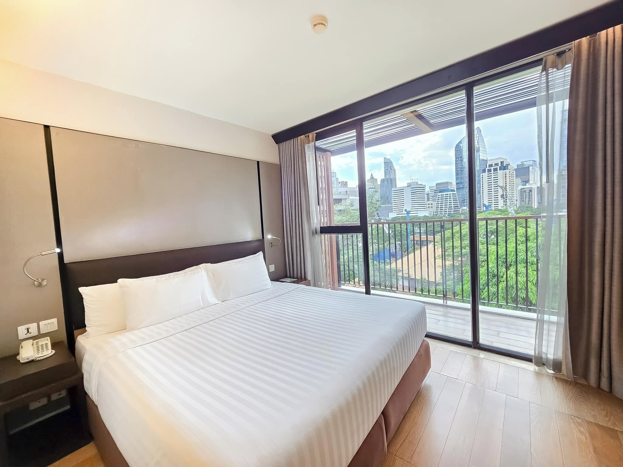 A hotel room with a large bed, a city view through floor-to-ceiling windows, and a modern design.