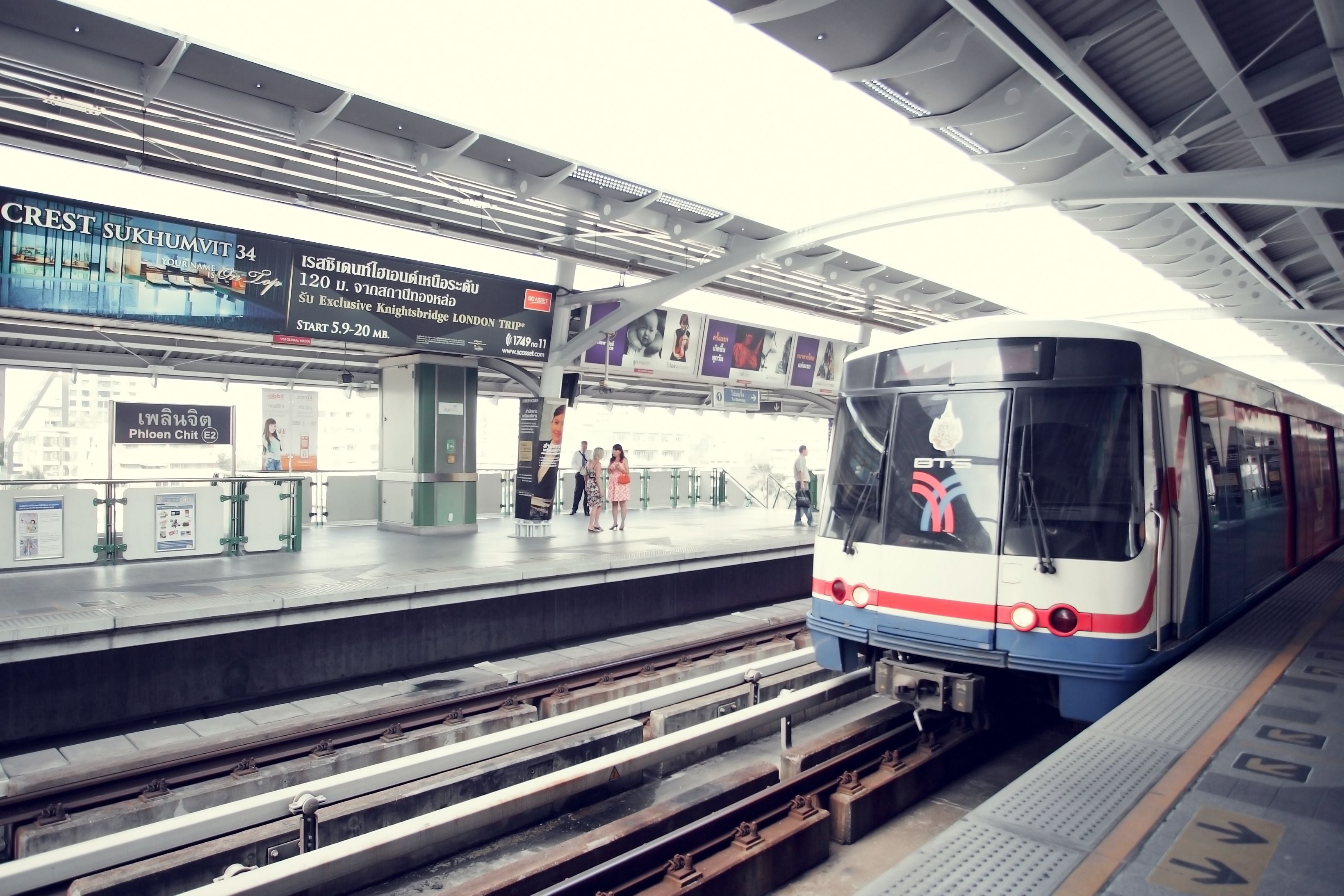 A train station platform with a modern train, overhead signs, and a clear view of the tracks.