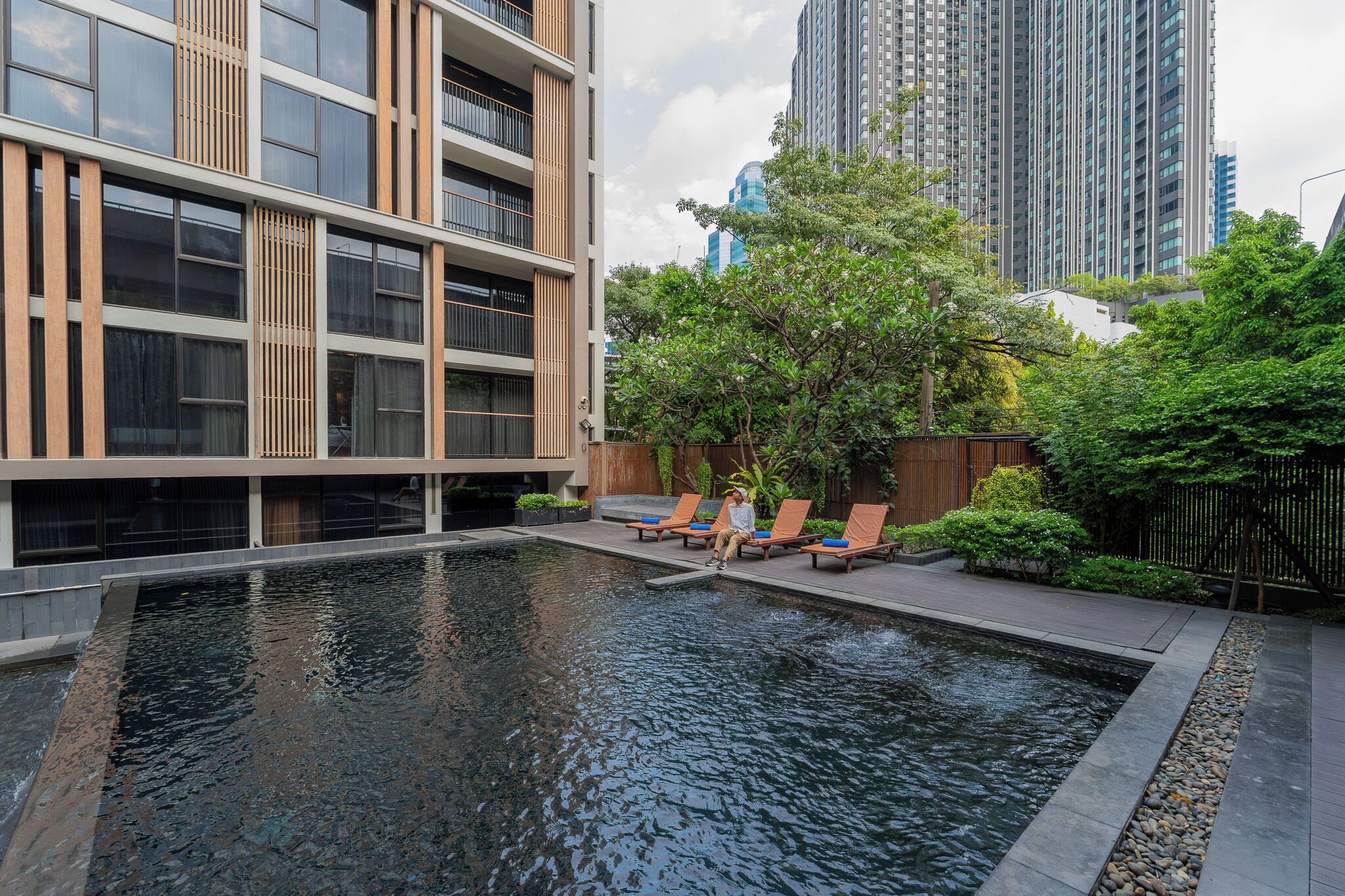 A modern building with a pool area, outdoor seating, and a view of tall buildings in the background.