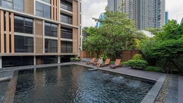 A modern building with a pool area, outdoor seating, and a view of tall buildings in the background.
