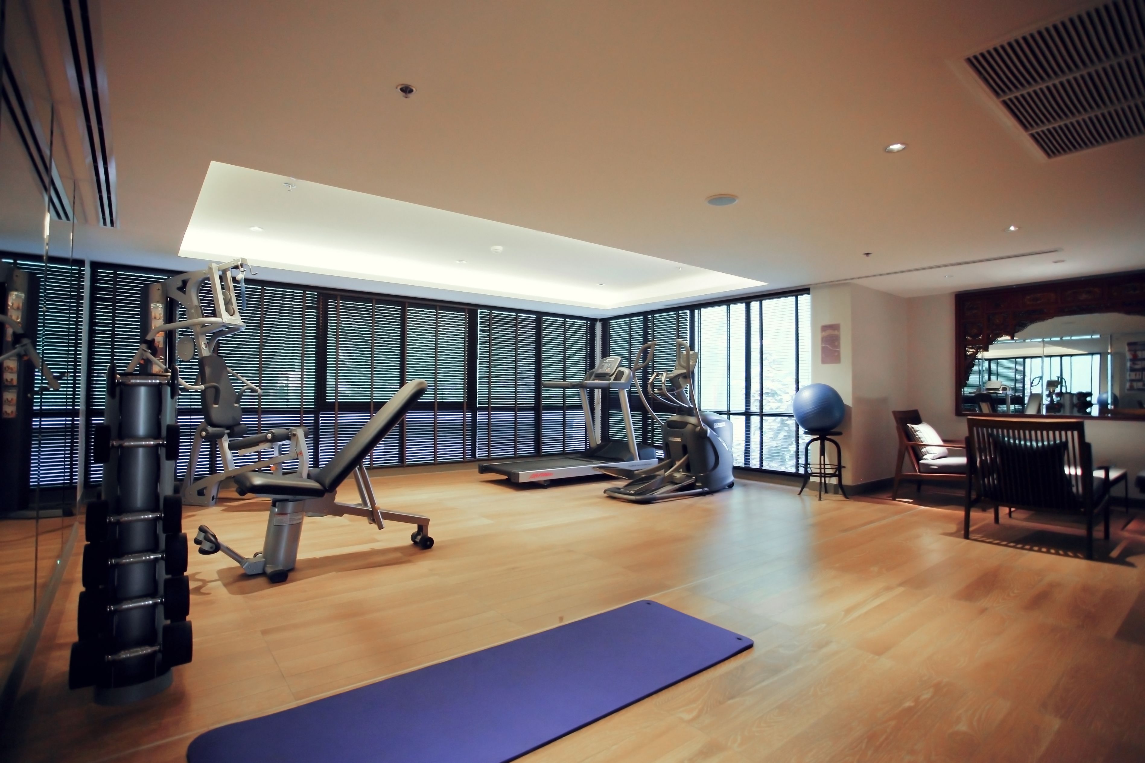 Ein großzügiger Fitnessraum mit unterschiedlichen Trainingsgeräten, großen Fenstern und Holzboden.