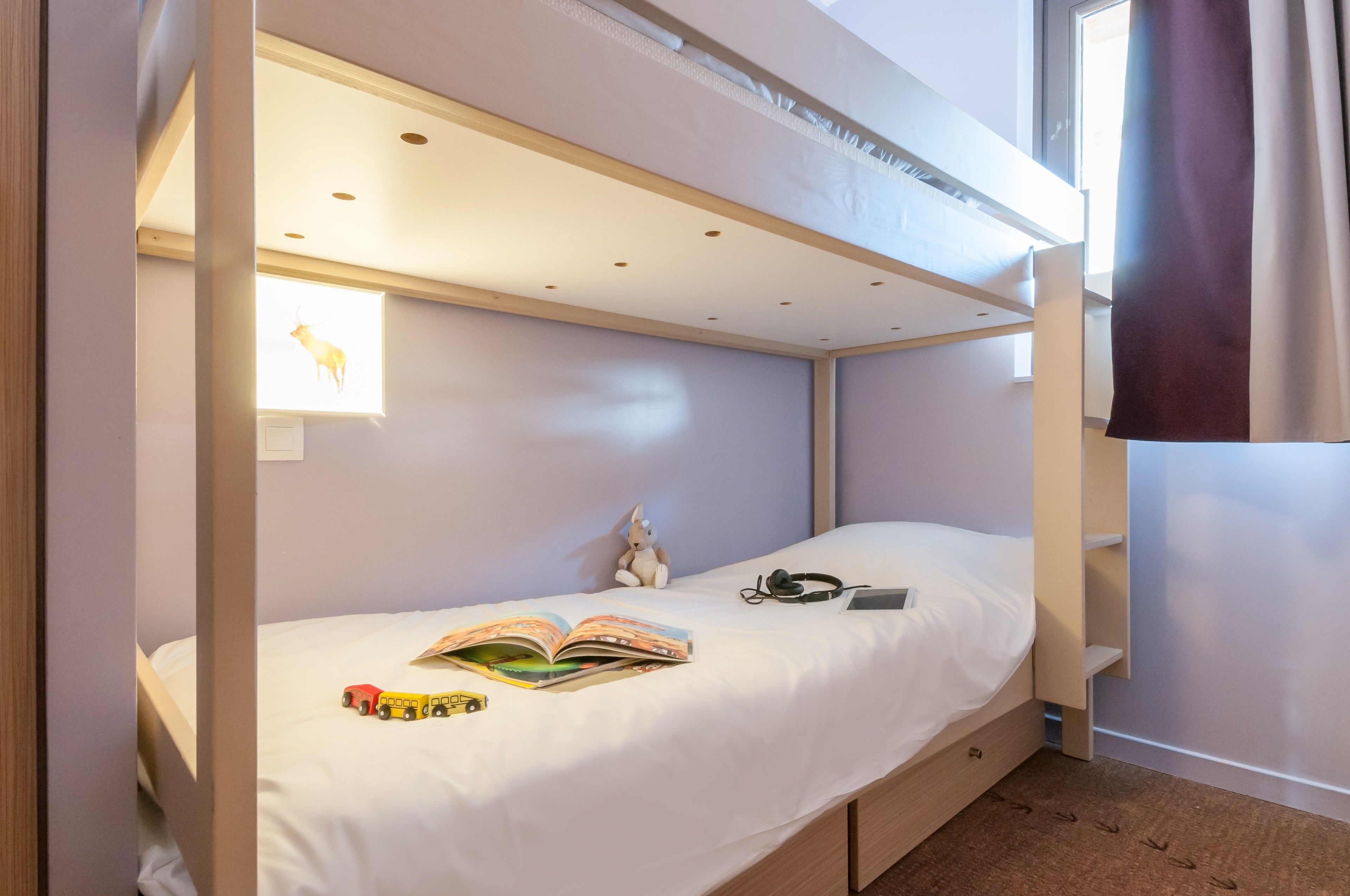 Een stapelbed met een witte matras, een pluchen speeltje, een boek en een treintje op het onderste bed.