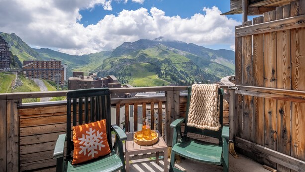 Una terraza de madera con dos sillas, una con un cojín con forma de copo de nieve, y una bandeja con una bebida. Se aprecia una vista de la montaña al fondo.