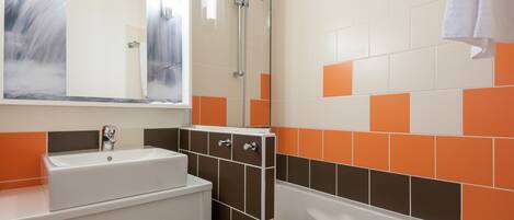 Een badkamer met een wit wastafelmeubel, een douche en een bad. De wanden zijn betegeld met oranje en witte tegels.