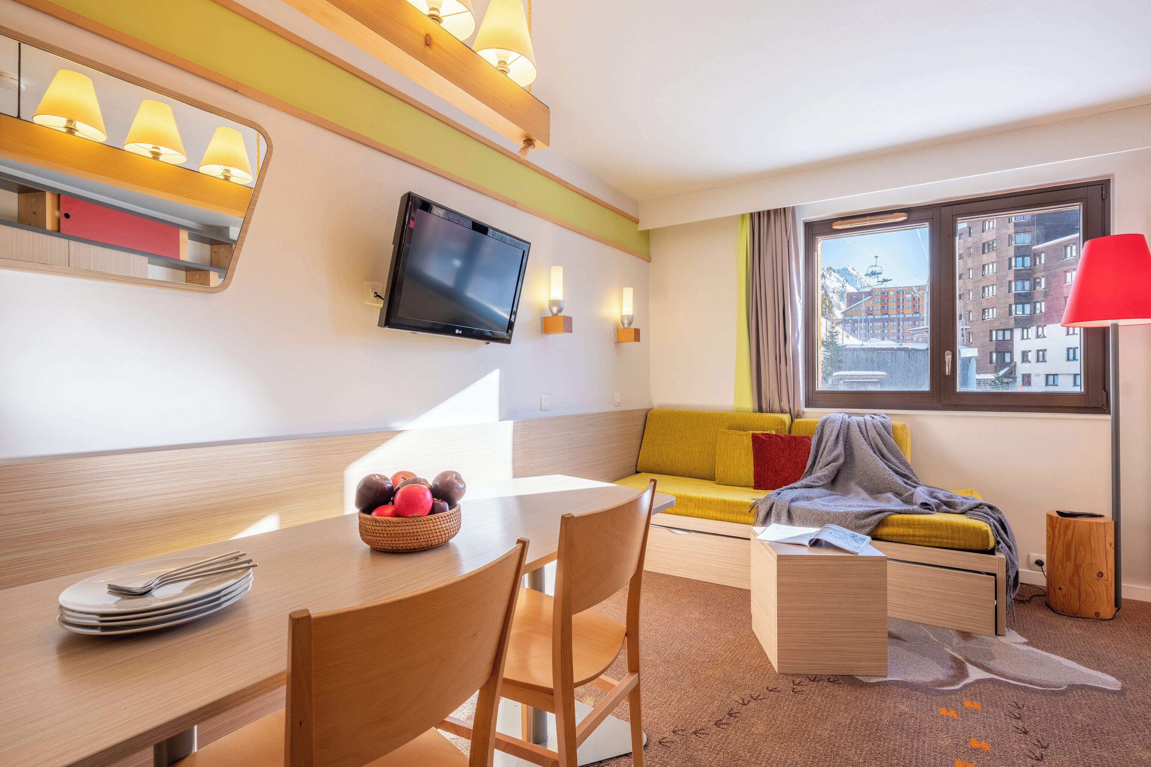 Une chambre d’hôtel moderne dotée d’un coin repas, d’un canapé, d’une télévision et d’une fenêtre donnant sur des immeubles.