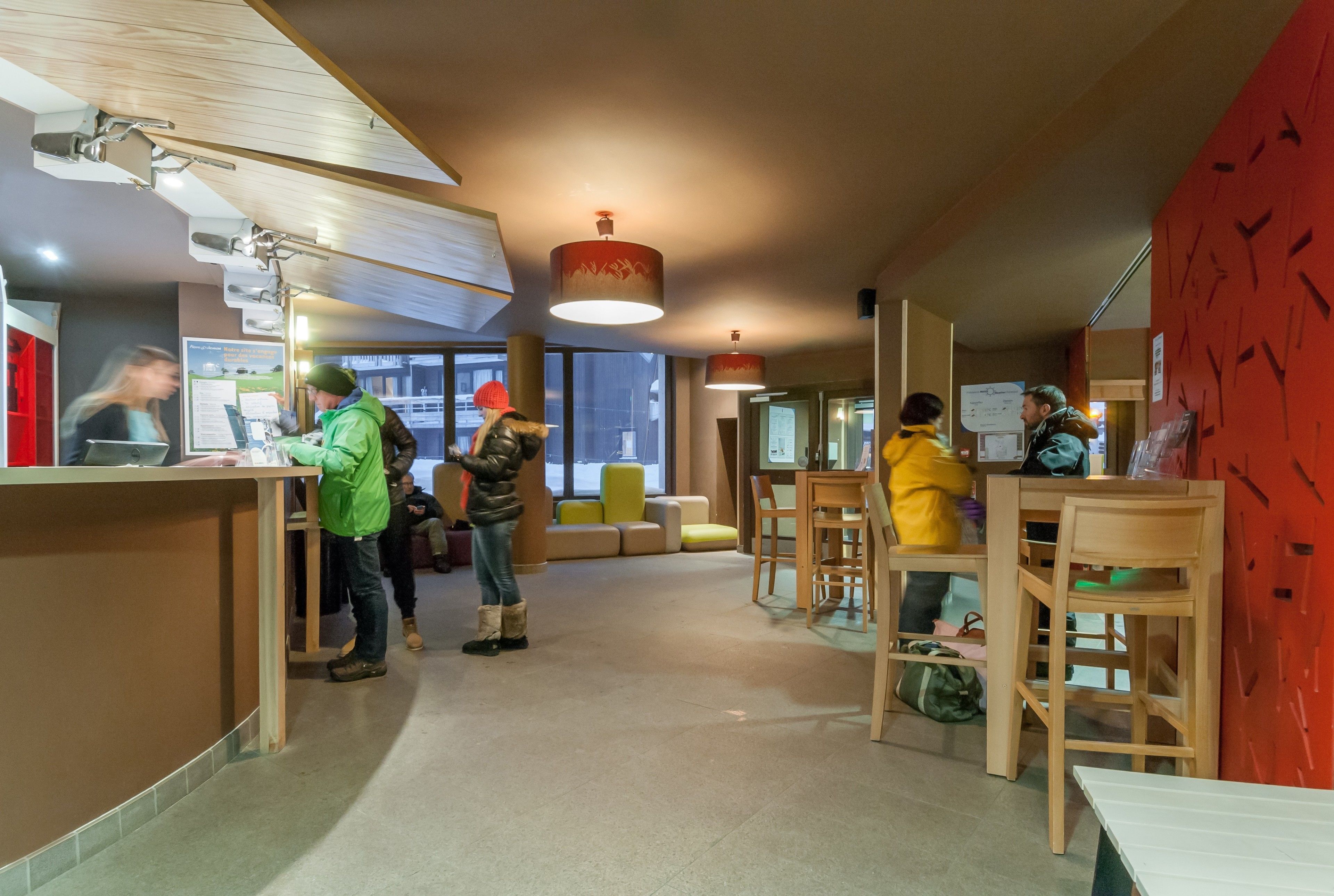 Un intérieur moderne comprenant un comptoir d’accueil, des espaces de détente et un mur d’accent rouge.