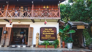 Ein traditionelles Holzhaus mit Balkon, einem Schild für das MyLaoHome Orchid House Hotel und Blumentöpfen.
