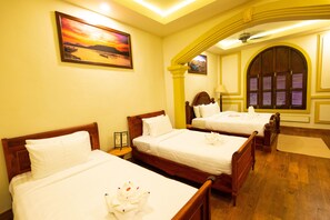 A hotel room with three wooden beds, each with white linens and towels. There is a painting on the wall and a large arched window with shutters. - Mylaohome Hotel & Spa (Luang Prabang)
