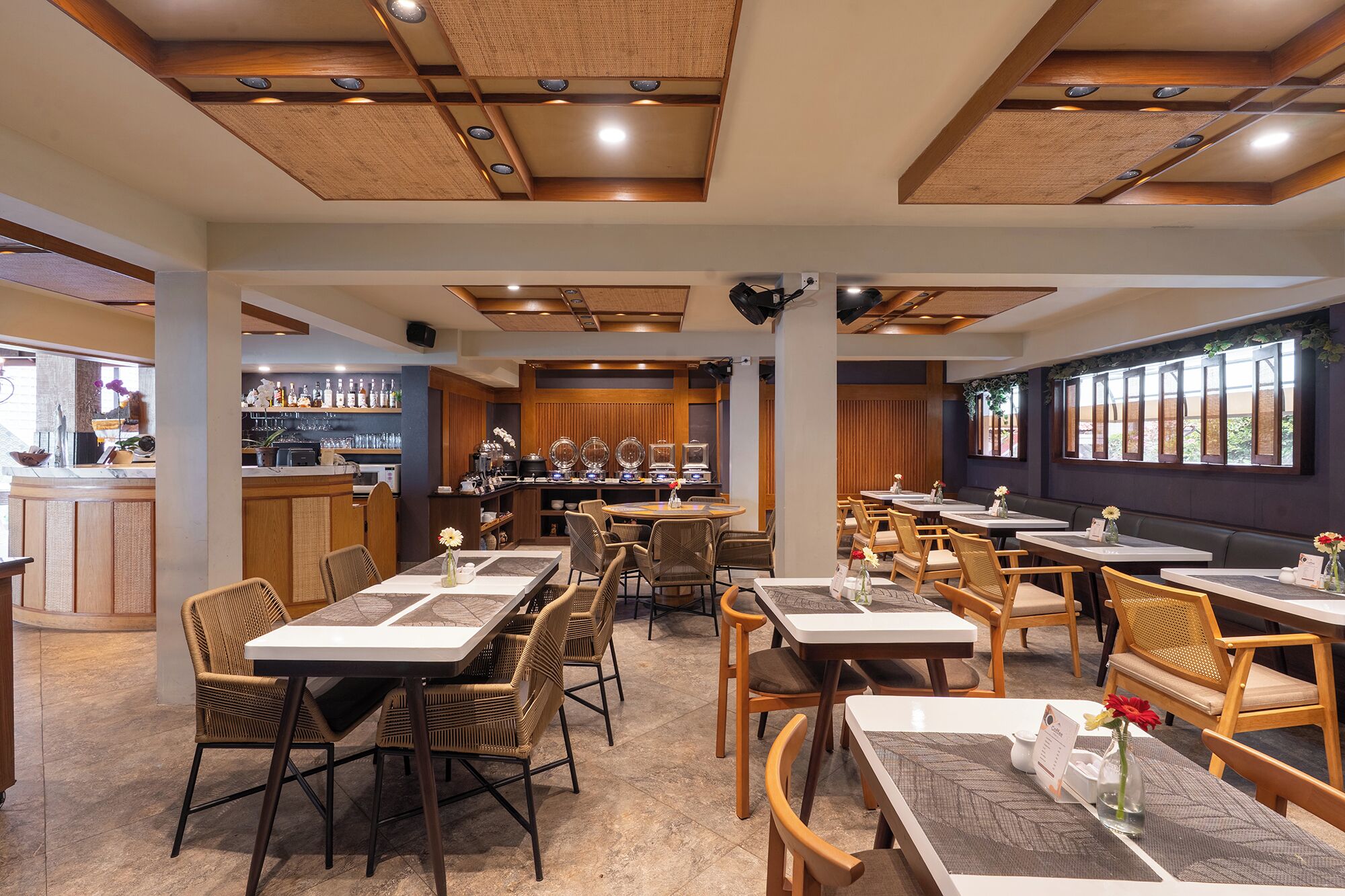 Un restaurante con paneles de madera en el techo, mesas con sillas, una zona de bar y amplios ventanales.