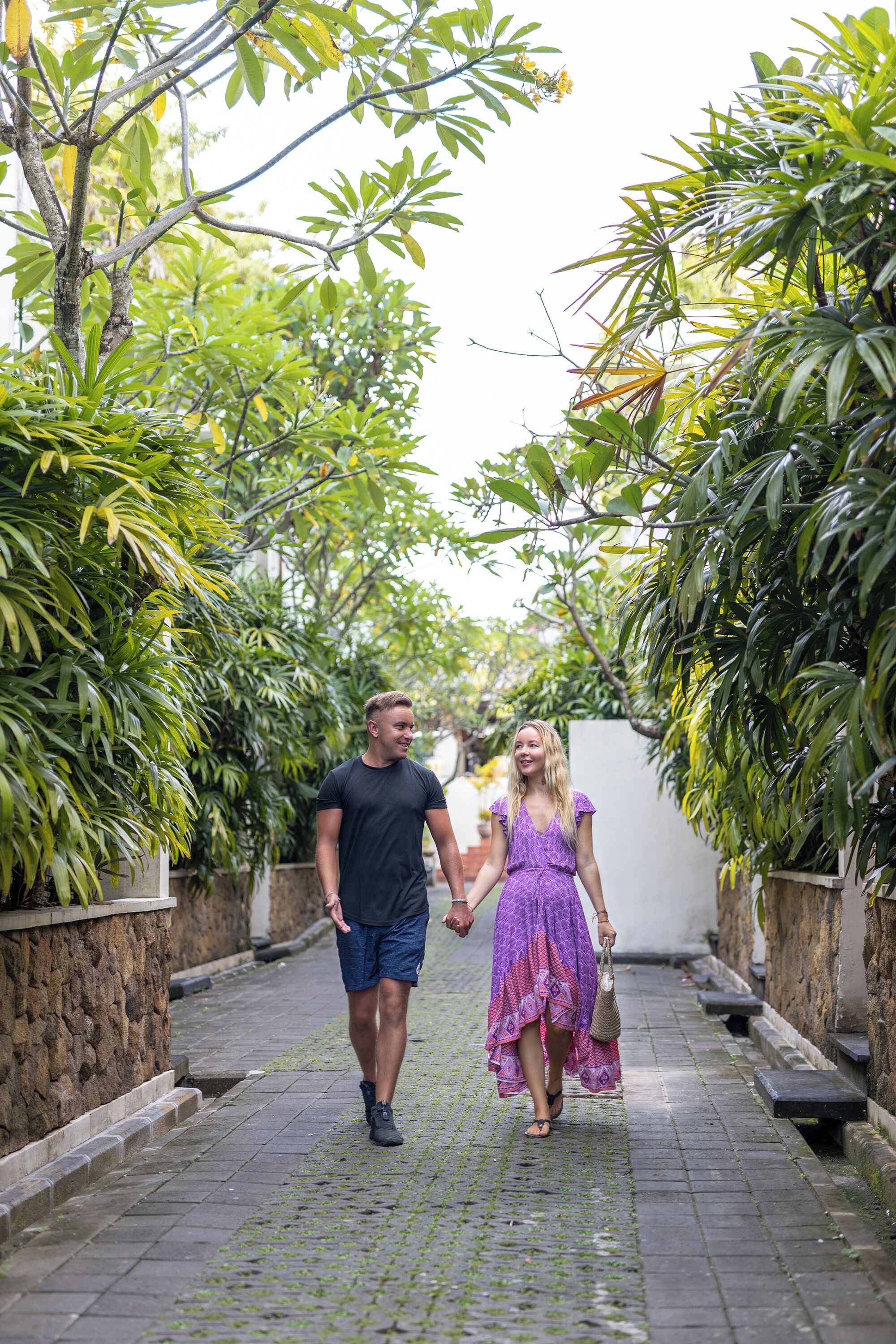 A couple walking on a cobblestone path flanked by lush greenery and stone walls.
