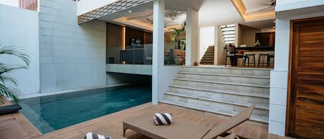 Un espace piscine extérieur moderne, doté de chaises longues et d’un escalier menant à un niveau supérieur.