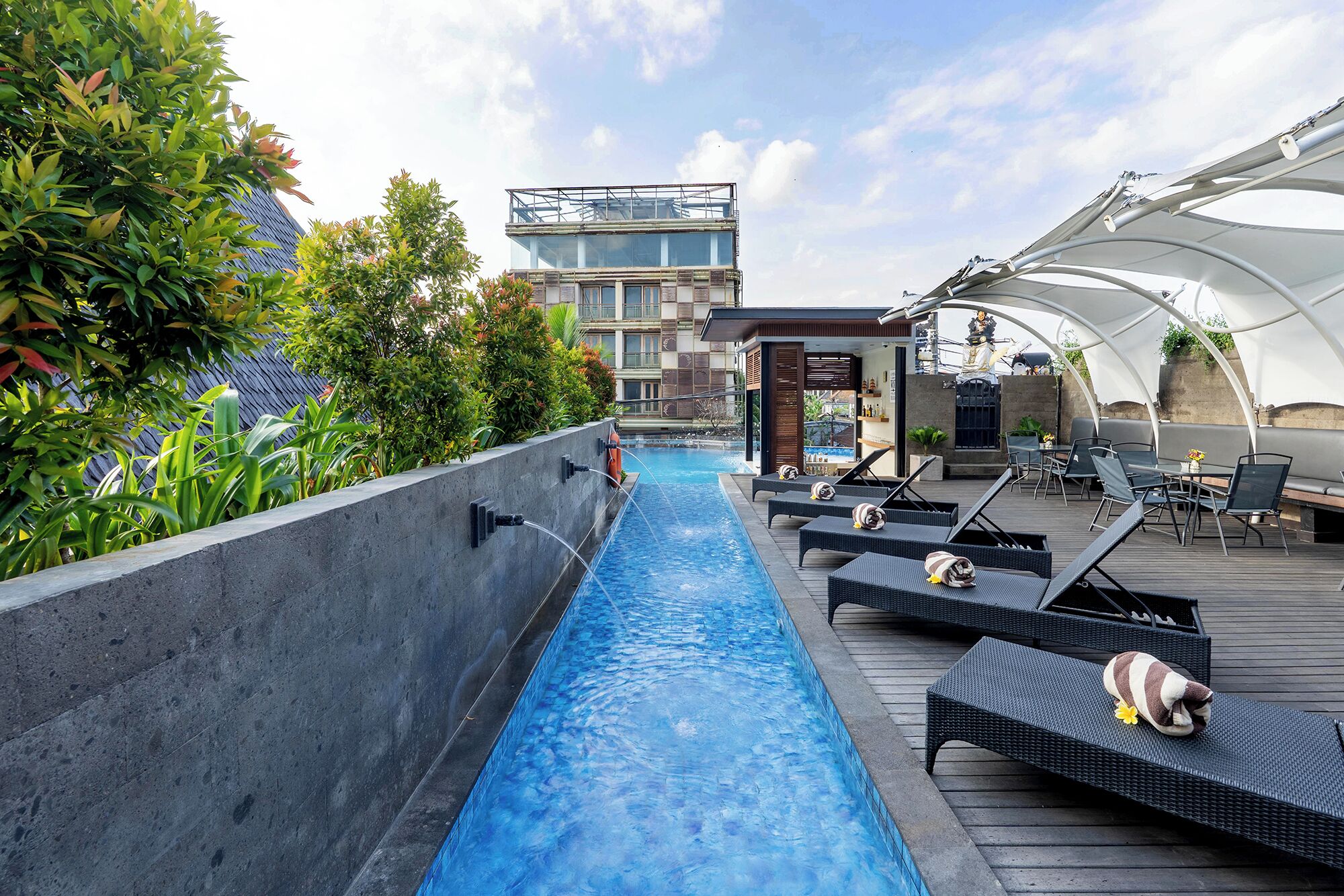 Un espace piscine aménagé sur le toit, avec des chaises longues, un bar et une vue sur un immeuble moderne.