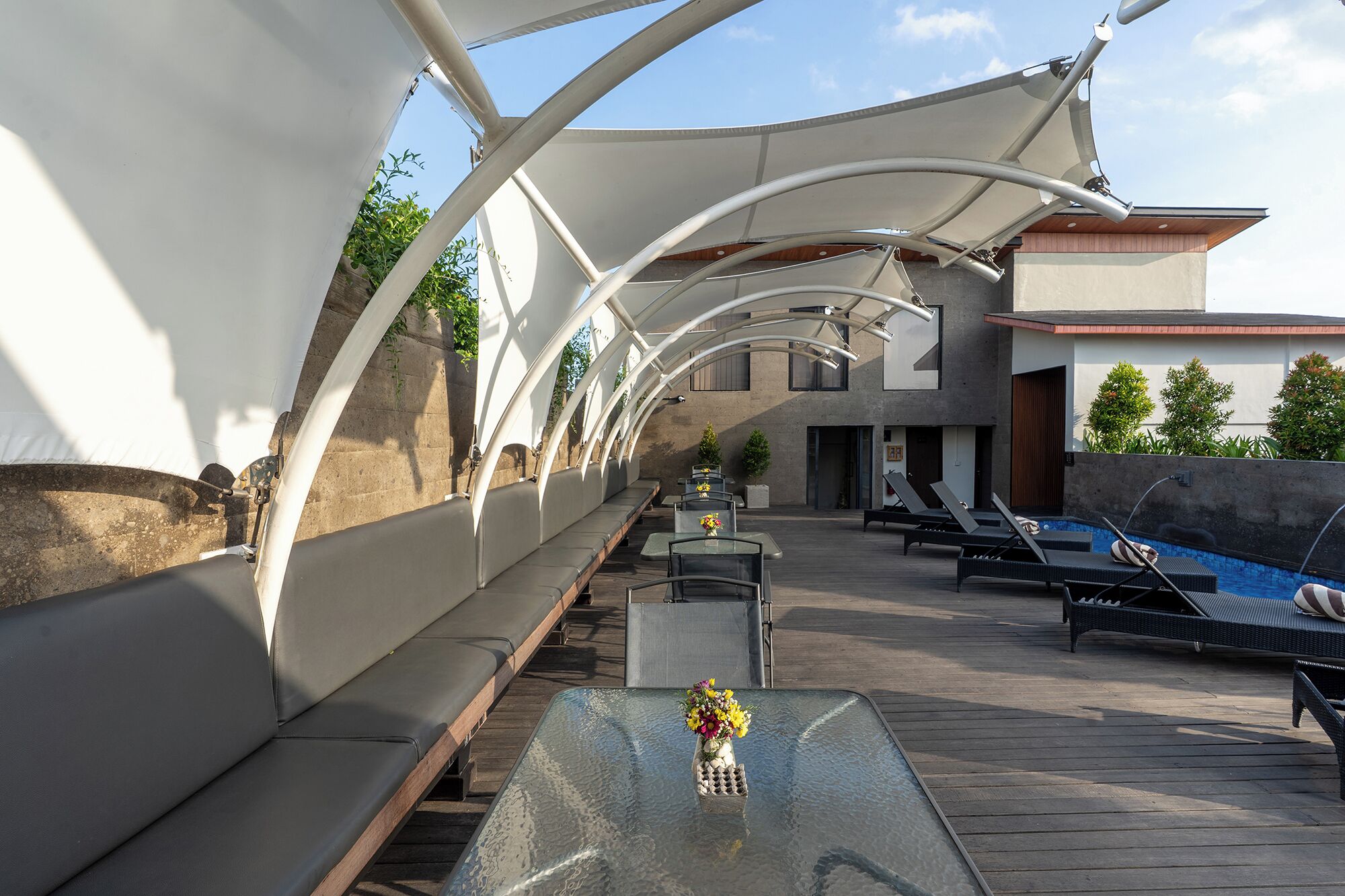 A sunlit outdoor seating area with tables and chairs, a pool, and a modern building in the background.