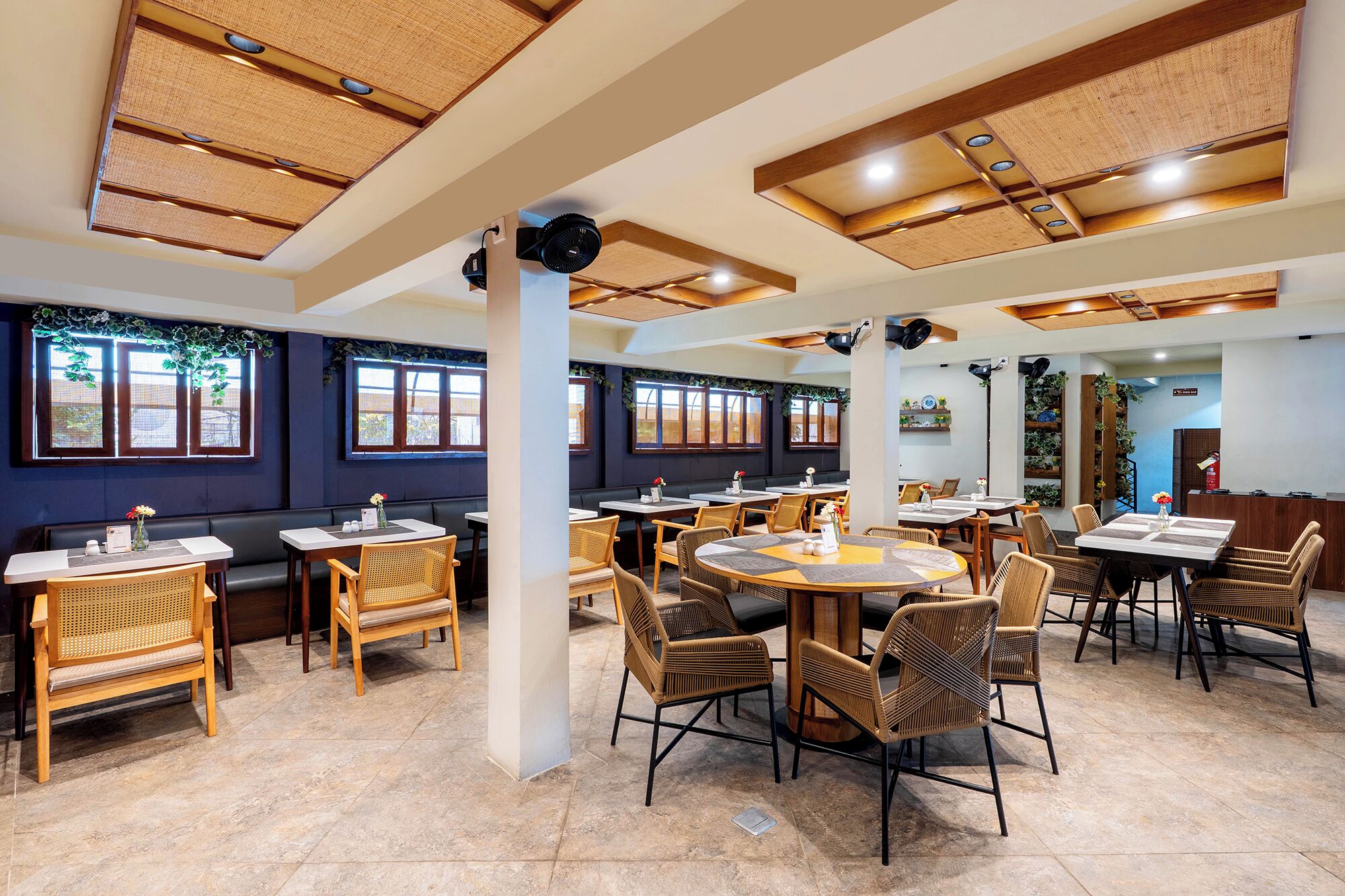 A restaurant with multiple tables and chairs, large windows, and a ceiling with woven panels.