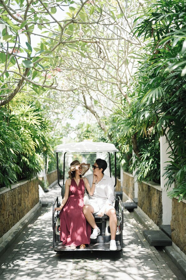 Una pareja conduce en un coche descapotable por un estrecho camino bordeado de árboles.
