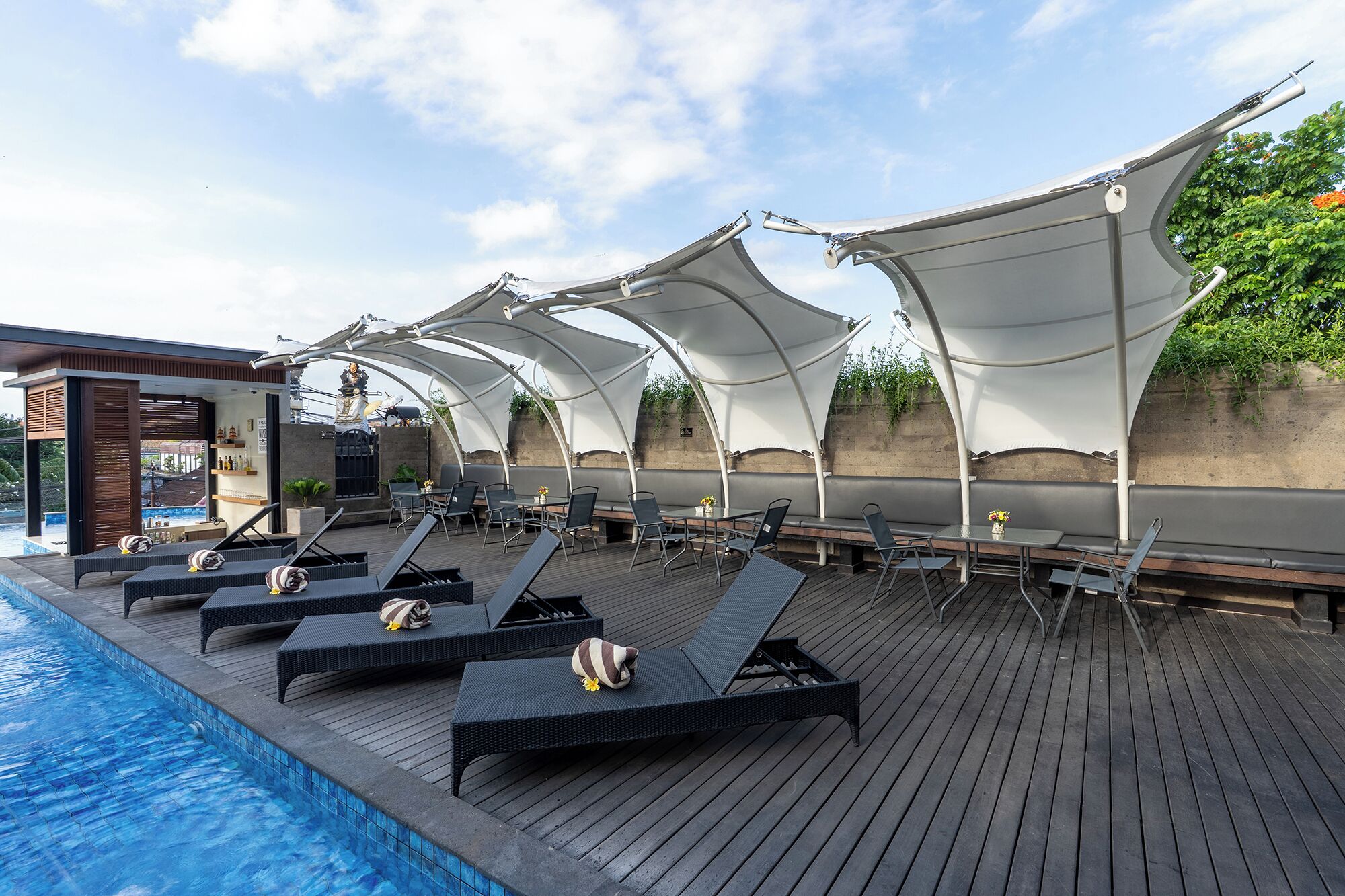 A poolside area with lounge chairs and umbrellas, a bar, and a statue.