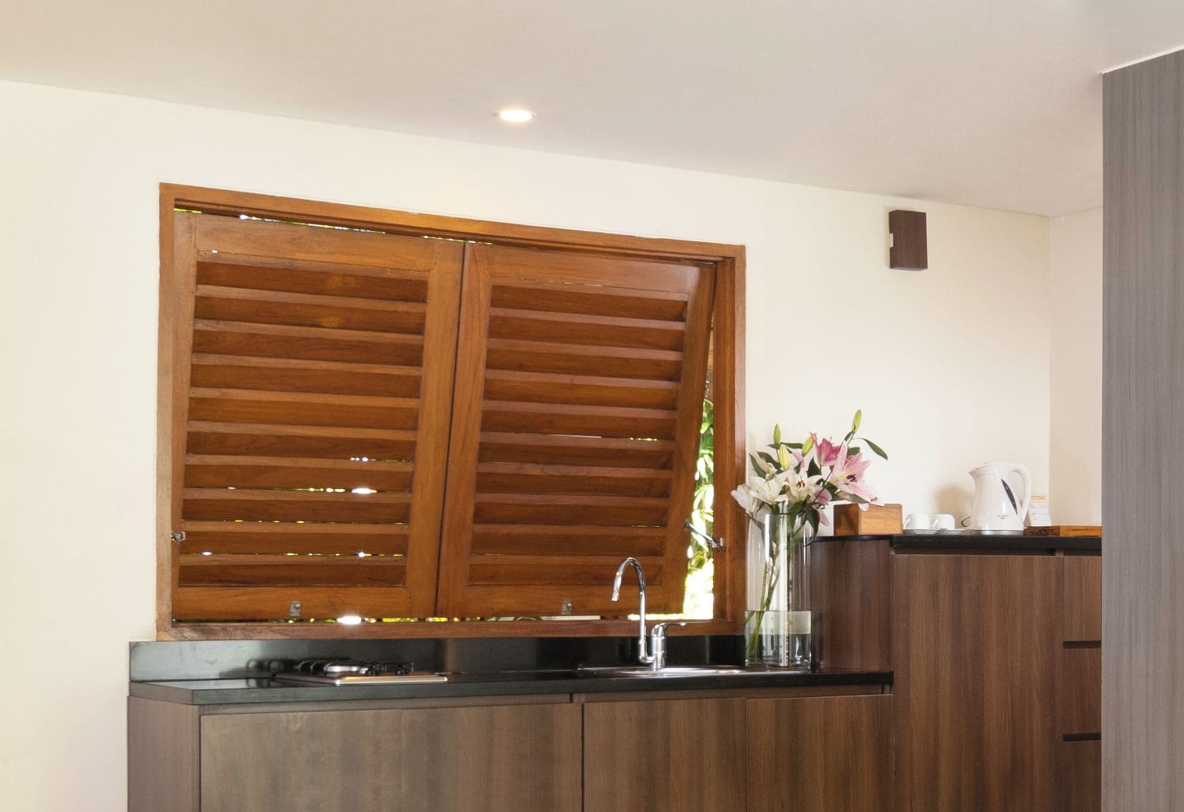 A kitchen with a wooden window, a sink, and a vase with flowers.