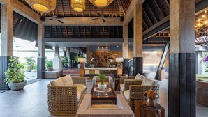 A spacious lobby with wicker furniture, a central seating area, and a large wooden sculpture. - Villa Kayu Raja (Seminyak)