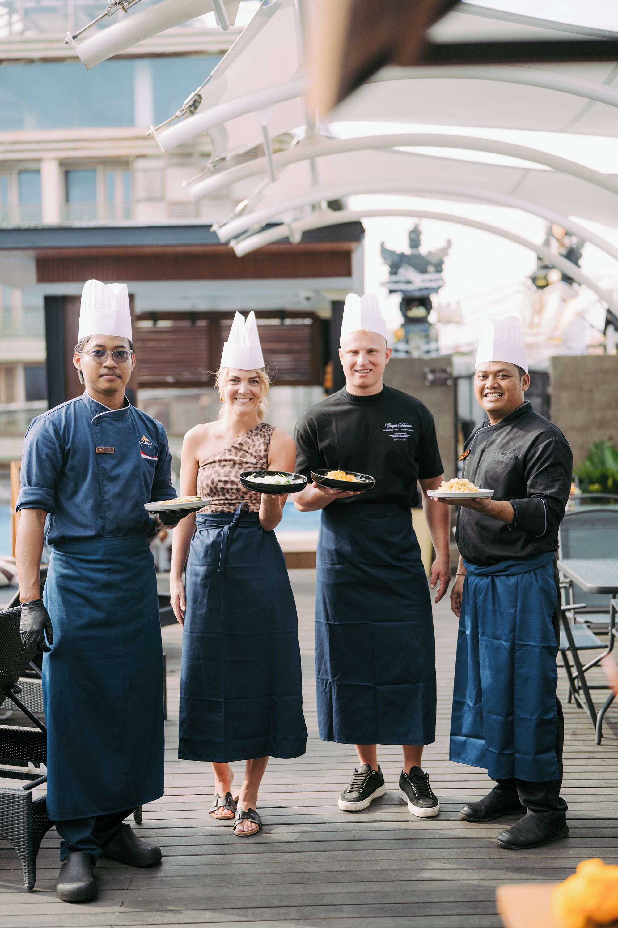 Four people in chef uniforms holding plates of food.