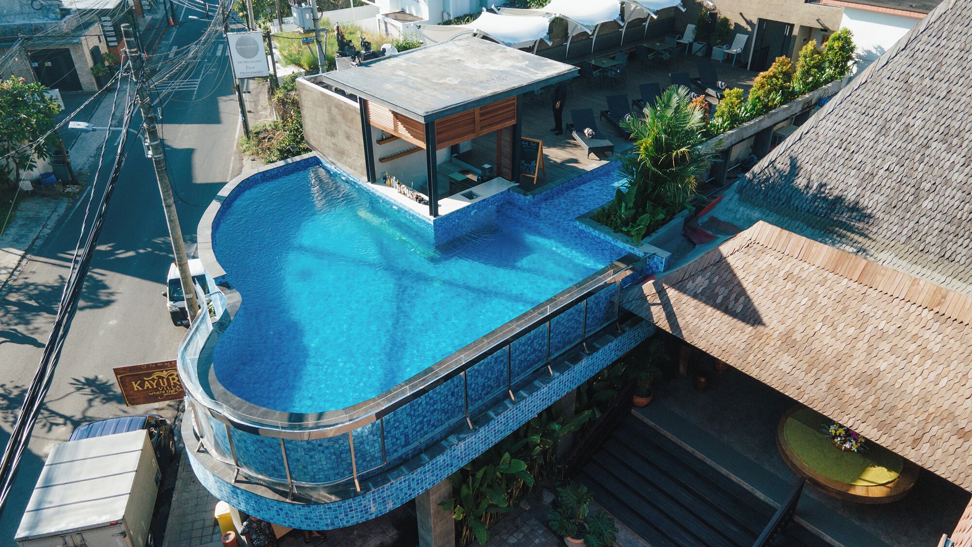 A rooftop swimming pool with a curved design, surrounded by a wooden deck and potted plants.
