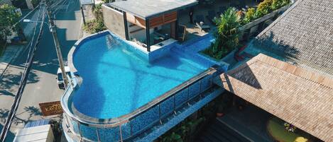 A rooftop swimming pool with a curved design, surrounded by a wooden deck and potted plants.