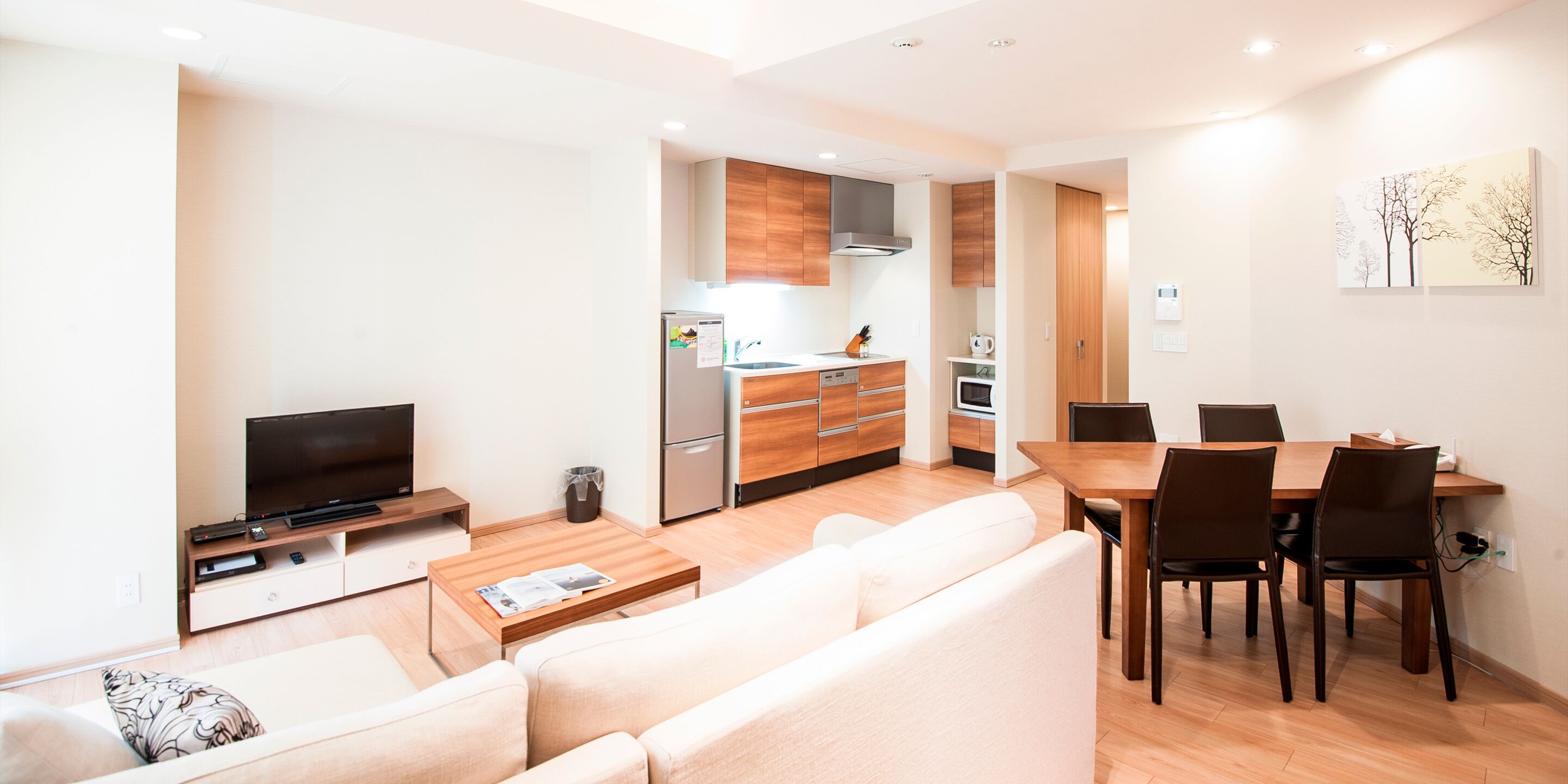 A modern living room with a sofa, coffee table, TV, and a dining area with chairs and a table.