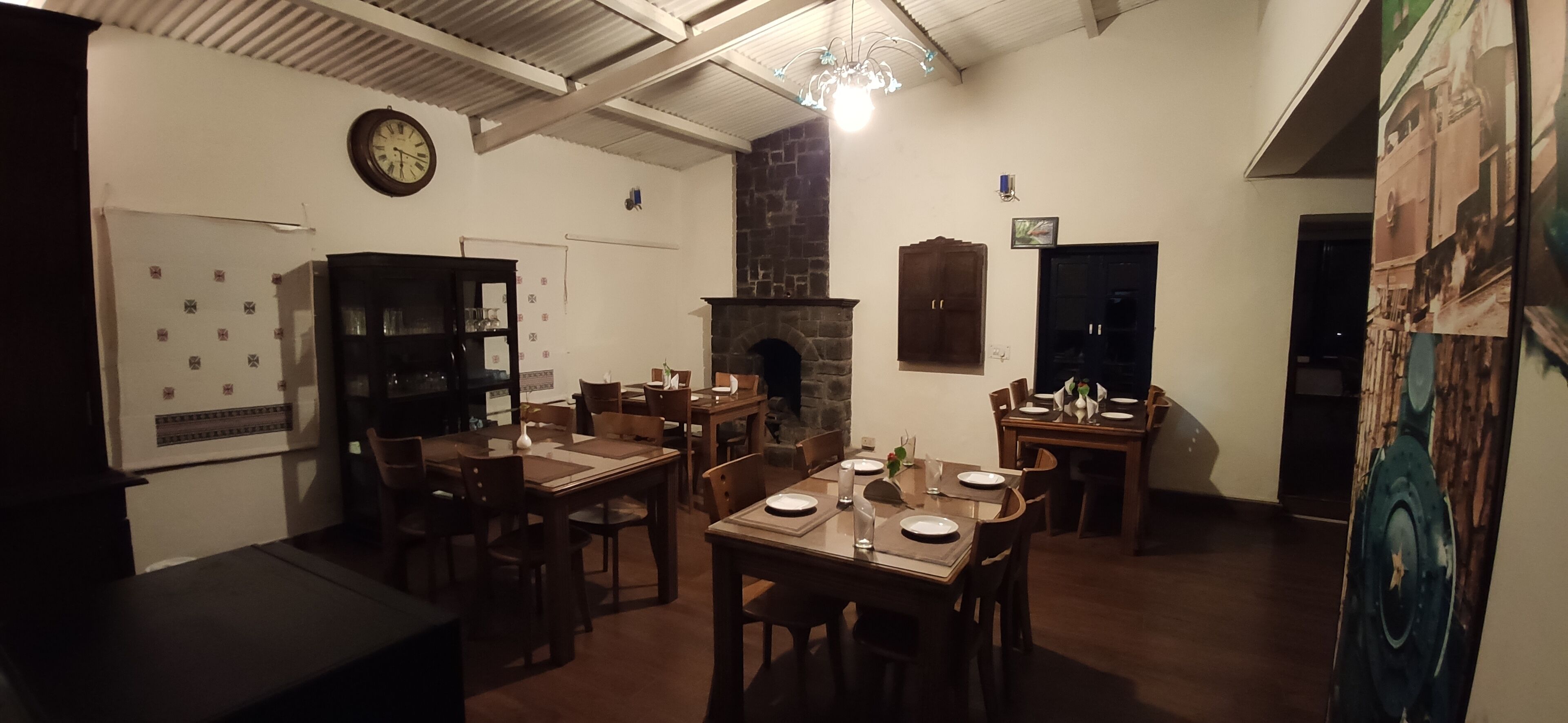 Un espace repas avec des tables et des chaises en bois, une horloge au mur et une cheminée.