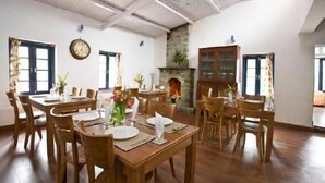 A dining area with wooden tables and chairs, a clock on the wall, and a fireplace. - I - India (Coonoor)