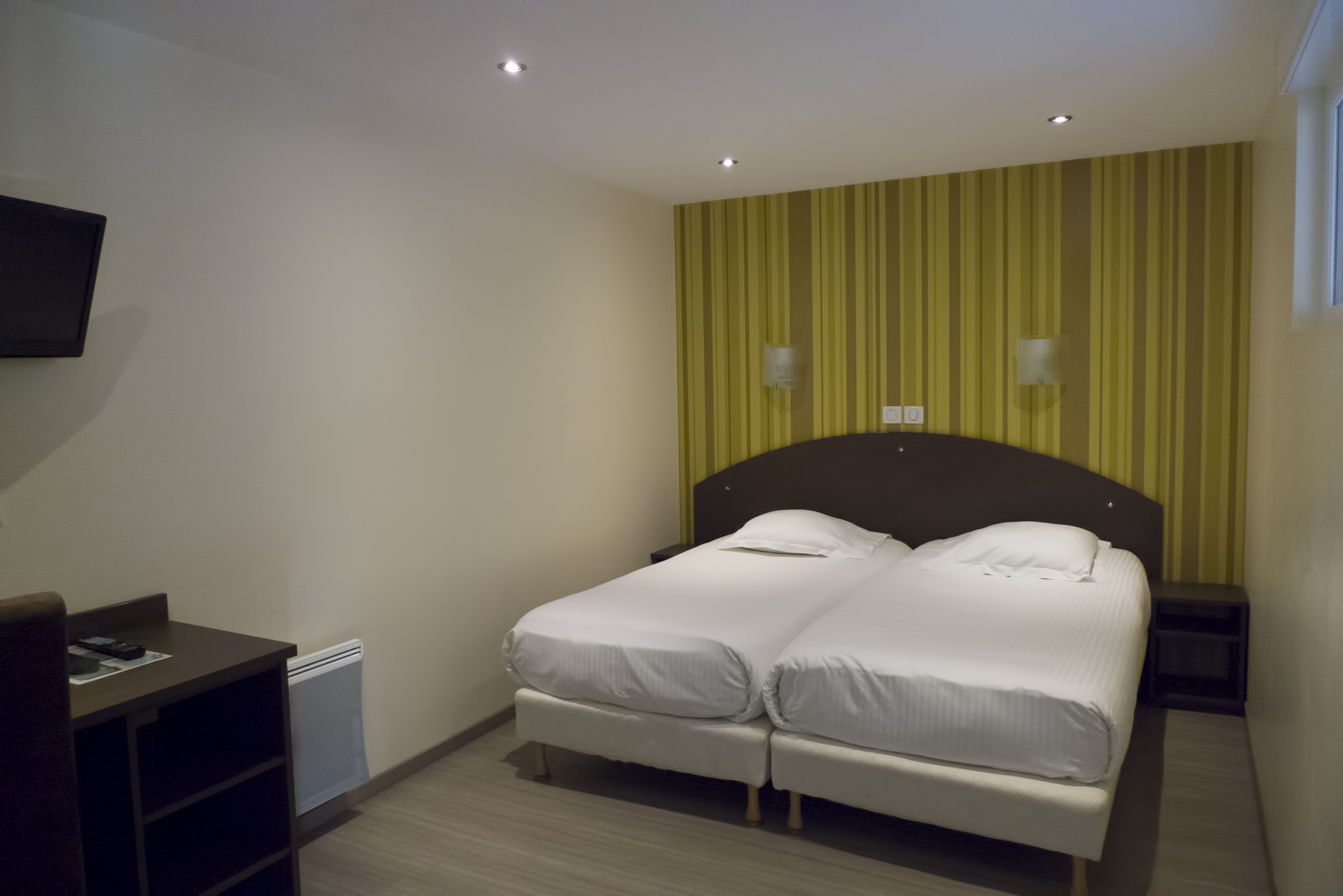 Una habitación de hotel con cama doble, escritorio y televisor en la pared.