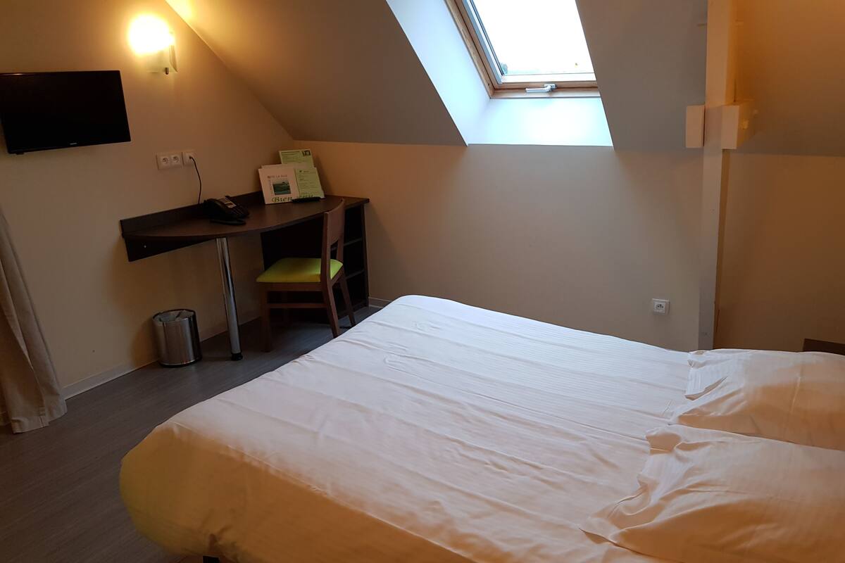 Una habitación con cama, escritorio, silla, cubo de basura y tragaluz.