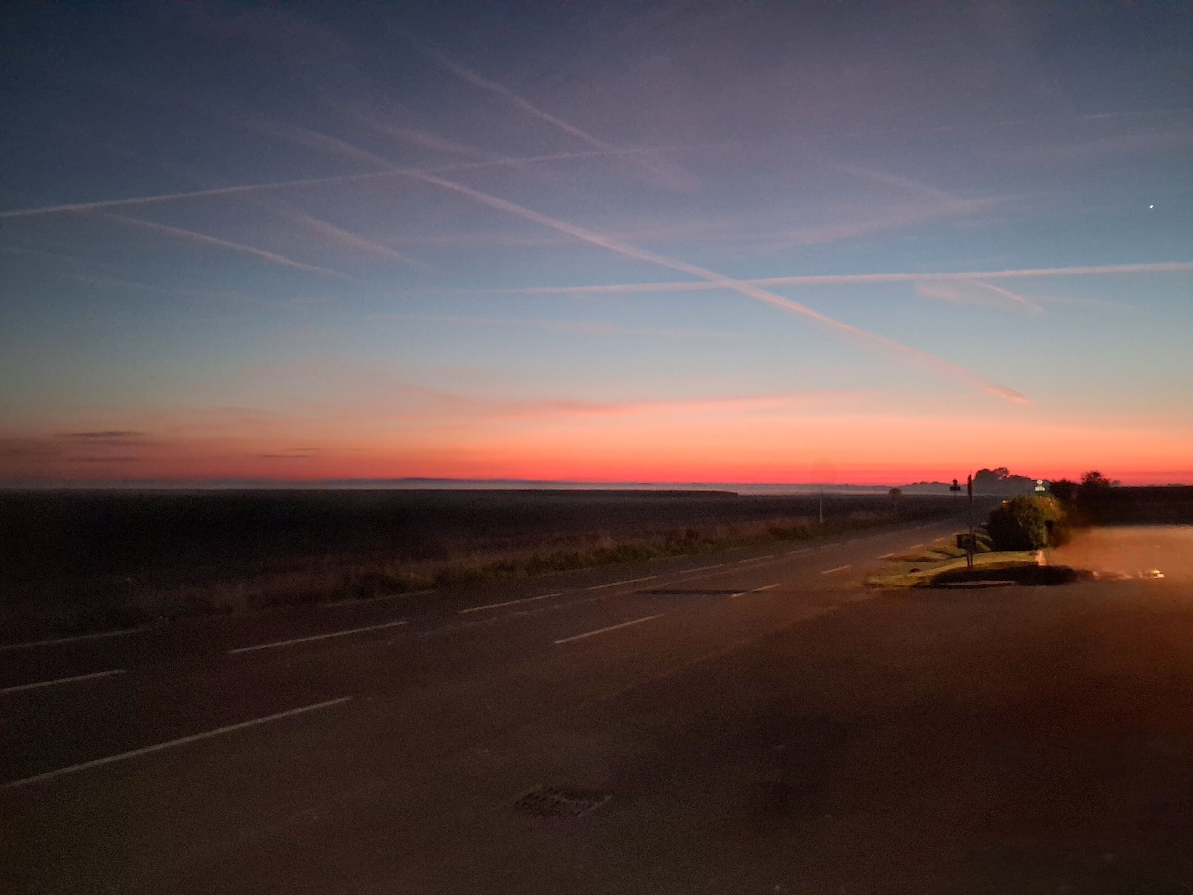 Carretera al atardecer con cielo despejado y horizonte lejano.