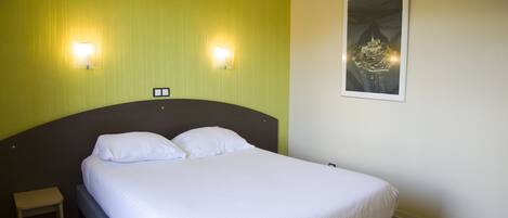 Una cama bien hecha en una habitación con paredes verdes, dos luces fijadas a la pared y un cuadro enmarcado.