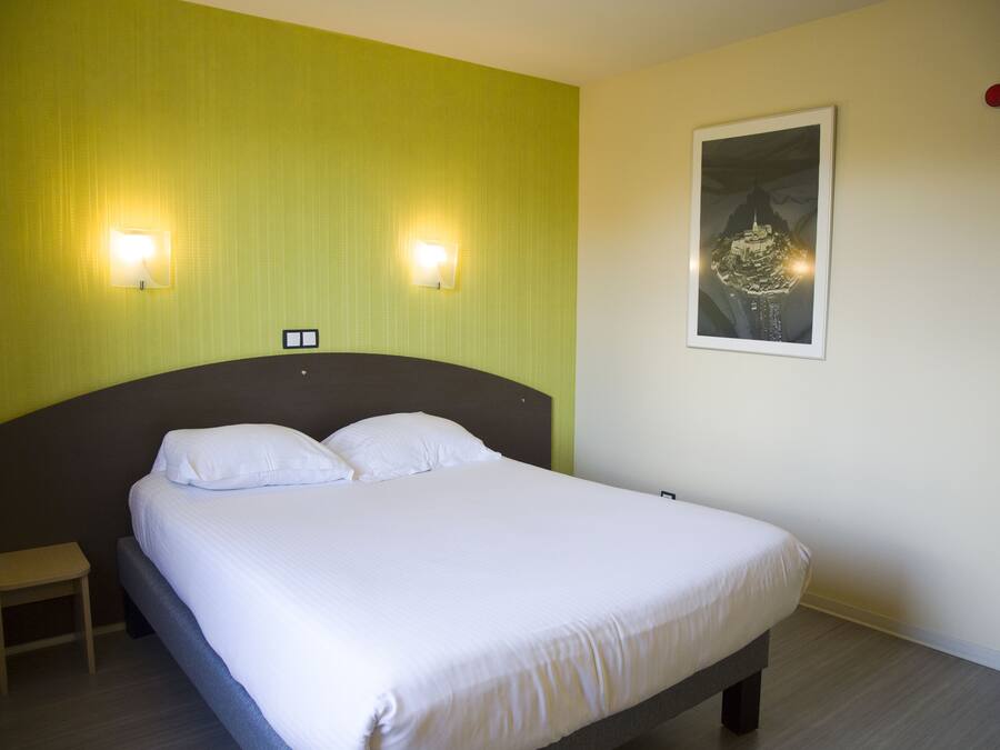 Una cama bien hecha en una habitación con paredes verdes, dos luces fijadas a la pared y un cuadro enmarcado.