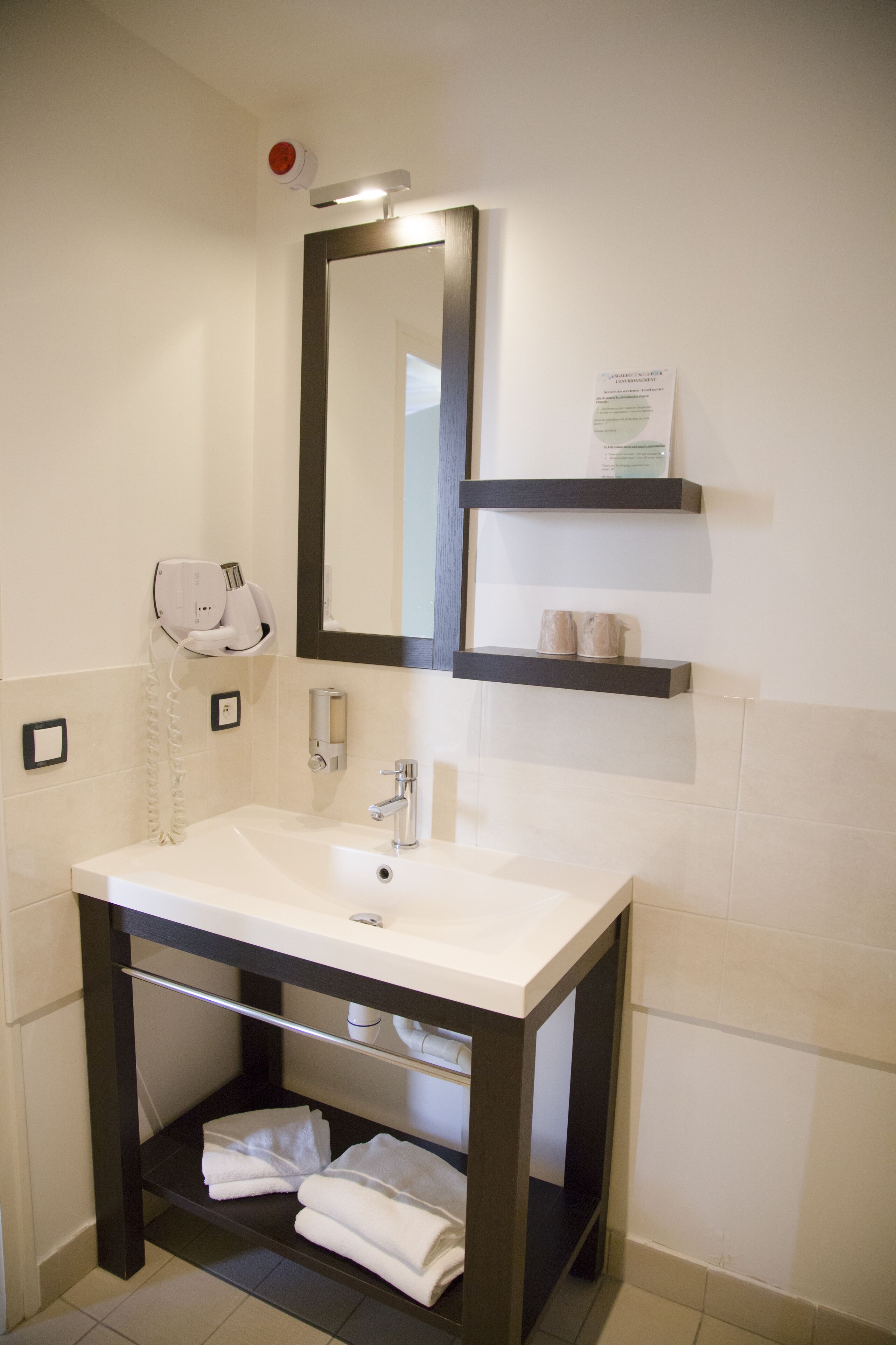 A modern bathroom with a white sink, a mirror, a towel rack, and a shelf with toiletries.