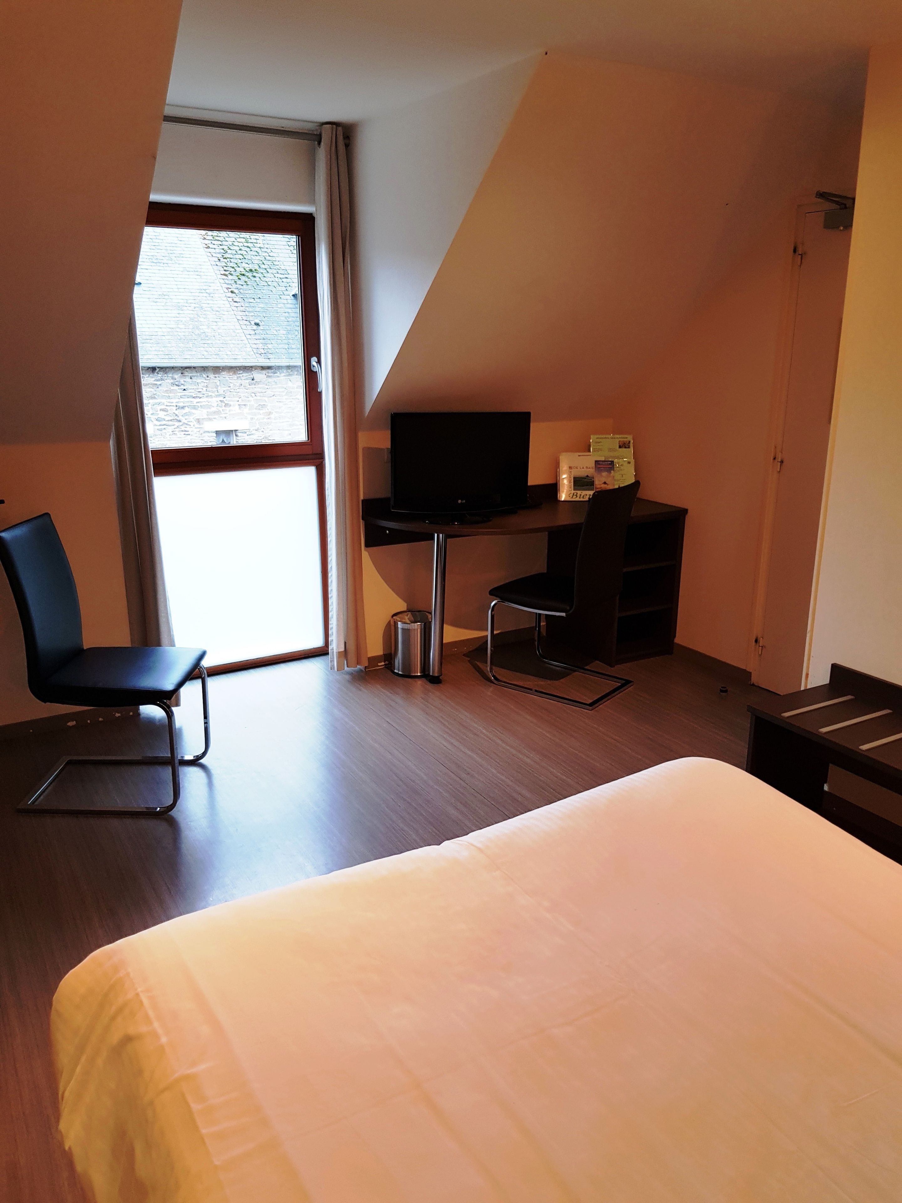Una camera d'albergo con un letto, una scrivania con un computer, una sedia e una finestra vista esterna.