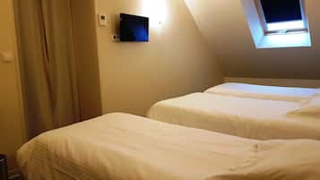A hotel room with two beds, a TV mounted on the wall, and a window with a view of the sky.
