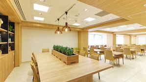 Un comedor amplio con mesas y sillas de madera, una jardinera central con plantas y lámparas colgantes.