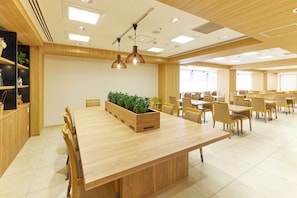 Un comedor amplio con mesas y sillas de madera, una jardinera central con plantas y lámparas colgantes.