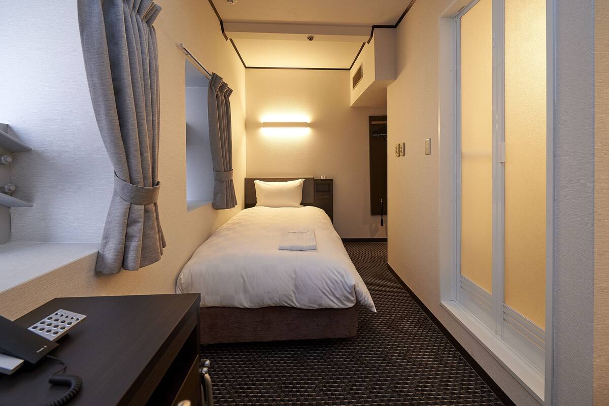Hotellihuone, jossa on sänky, yöpöytä ja työpöytä, jossa on puhelin.